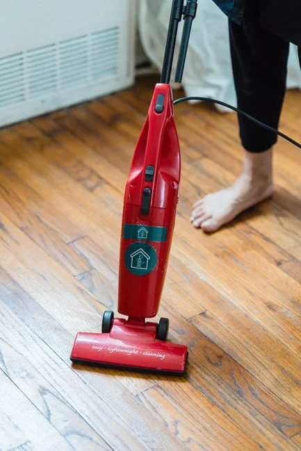 hero-img-02 Close-up of people cleaning wooden floor with broom and dustpan indoors.